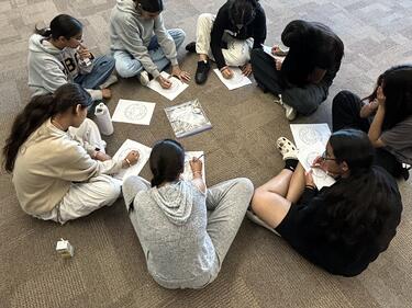 students sitting on floor in a circle, writing on paper