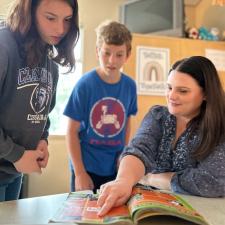 Teacher points at something in a book, while two students look at what it is.